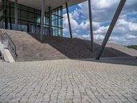 a person on a bike walking through a stone building entrance, in front of an enormous glass wall and stairs