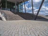 a person on a bike walking through a stone building entrance, in front of an enormous glass wall and stairs