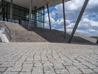 a person on a bike walking through a stone building entrance, in front of an enormous glass wall and stairs