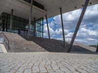 a person on a bike walking through a stone building entrance, in front of an enormous glass wall and stairs