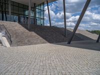 a person on a bike walking through a stone building entrance, in front of an enormous glass wall and stairs