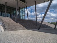 a person on a bike walking through a stone building entrance, in front of an enormous glass wall and stairs