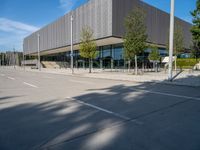 a metal building with several large trees in the foreground and some buildings near by