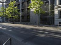 the side of a tall glass building with trees and benches in front of it in an urban area