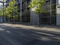 the side of a tall glass building with trees and benches in front of it in an urban area