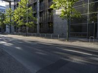 the side of a tall glass building with trees and benches in front of it in an urban area