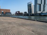 a brick walkway in front of tall buildings along a body of water in a city