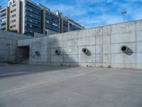 the empty parking lot in front of a wall with apartment buildings on it and a skateboarder on a ramp