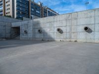 the empty parking lot in front of a wall with apartment buildings on it and a skateboarder on a ramp