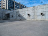 the empty parking lot in front of a wall with apartment buildings on it and a skateboarder on a ramp