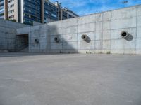 the empty parking lot in front of a wall with apartment buildings on it and a skateboarder on a ramp