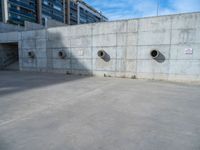 the empty parking lot in front of a wall with apartment buildings on it and a skateboarder on a ramp