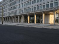 there is a long empty city street by the building, with tall columns on both sides of the street