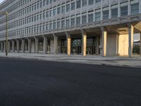 there is a long empty city street by the building, with tall columns on both sides of the street