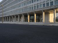 there is a long empty city street by the building, with tall columns on both sides of the street