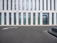 the side of an office building with windows on each floor and a large concrete oval shaped asphalt area