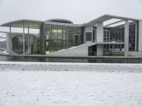 a large building sitting in the snow next to water, with people walking on the ice