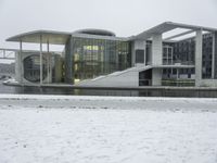 a large building sitting in the snow next to water, with people walking on the ice