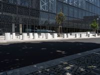 concrete street posts along the street side are lined with plants and trees in front of a glass building