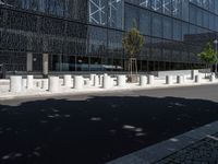 concrete street posts along the street side are lined with plants and trees in front of a glass building