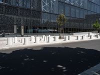 concrete street posts along the street side are lined with plants and trees in front of a glass building