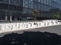 concrete street posts along the street side are lined with plants and trees in front of a glass building