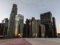 people walk near a deserted parking lot in a cityscape at dusk with some buildings