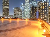 an area with a bench and firelight on top of it at night with the city lights turned on