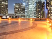 an area with a bench and firelight on top of it at night with the city lights turned on