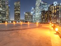 an area with a bench and firelight on top of it at night with the city lights turned on