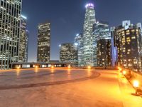 an area with a bench and firelight on top of it at night with the city lights turned on