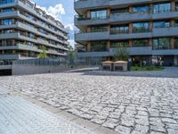 the empty bench is near an outdoor courtyard area of a large building with high rise apartment buildings