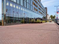 the sidewalk in front of an office building is empty except the sidewalk in front of the building is lined with bricks