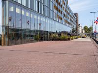 the sidewalk in front of an office building is empty except the sidewalk in front of the building is lined with bricks