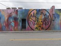 a colorful building that is painted with various colors and graffiti written across it and a clock on the side