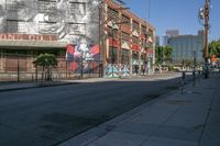 a view down an empty street towards a building with graffiti and another mural on it