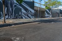 the man on a skateboard is in the street by a mural of elephants on the building's side