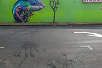 colorful mural of lizard in the middle of an intersection with liquor store sign and trees