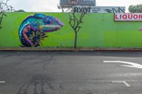 colorful mural of lizard in the middle of an intersection with liquor store sign and trees