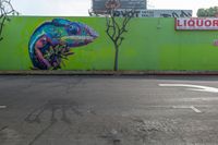 colorful mural of lizard in the middle of an intersection with liquor store sign and trees