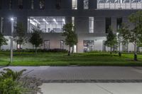 a large courtyard with a grassy area at night in the background is a modern office building