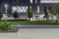 a large courtyard with a grassy area at night in the background is a modern office building