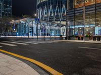 an empty city street next to the entrance of a tall building in the night time