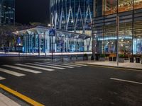 an empty city street next to the entrance of a tall building in the night time