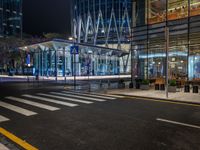 an empty city street next to the entrance of a tall building in the night time