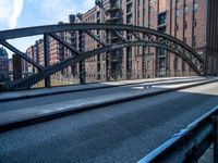 a street with a train track leading to a brick building across it is bridge in the center of the picture, and buildings and an alley along a road in front