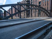 a street with a train track leading to a brick building across it is bridge in the center of the picture, and buildings and an alley along a road in front