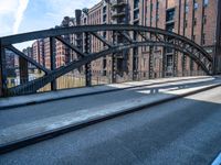 a street with a train track leading to a brick building across it is bridge in the center of the picture, and buildings and an alley along a road in front