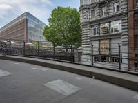 the woman is walking her bike down the city street along the railing with another man sitting on a bench behind her