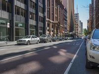 a street filled with parked cars and tall buildings next to it's sidewalk with a bike rack